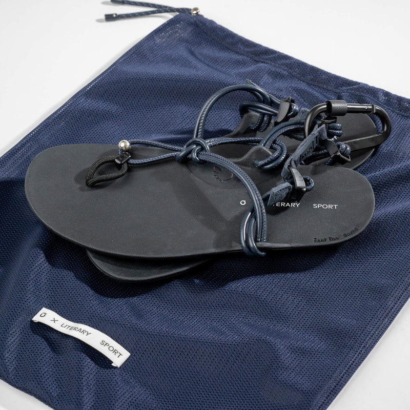 Xero Shoes Literary Sport Genesis Navy Strap Black Sandal with an Elevated View Showing Both Sandals Placed Directly on Top of the Navy Mesh Storage Bag.