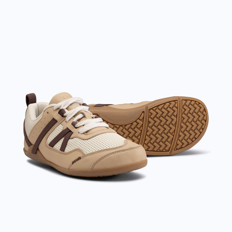 A Pair of Xero Shoes Prio Leather Sneakers in Cream and Brown. One Shoe Faces Forward Toward the Bottom Right, While the Other Shoe Sits Behind it, Flipped to Showcase its Textured Rubber Outsole and with Toe Facing Right.